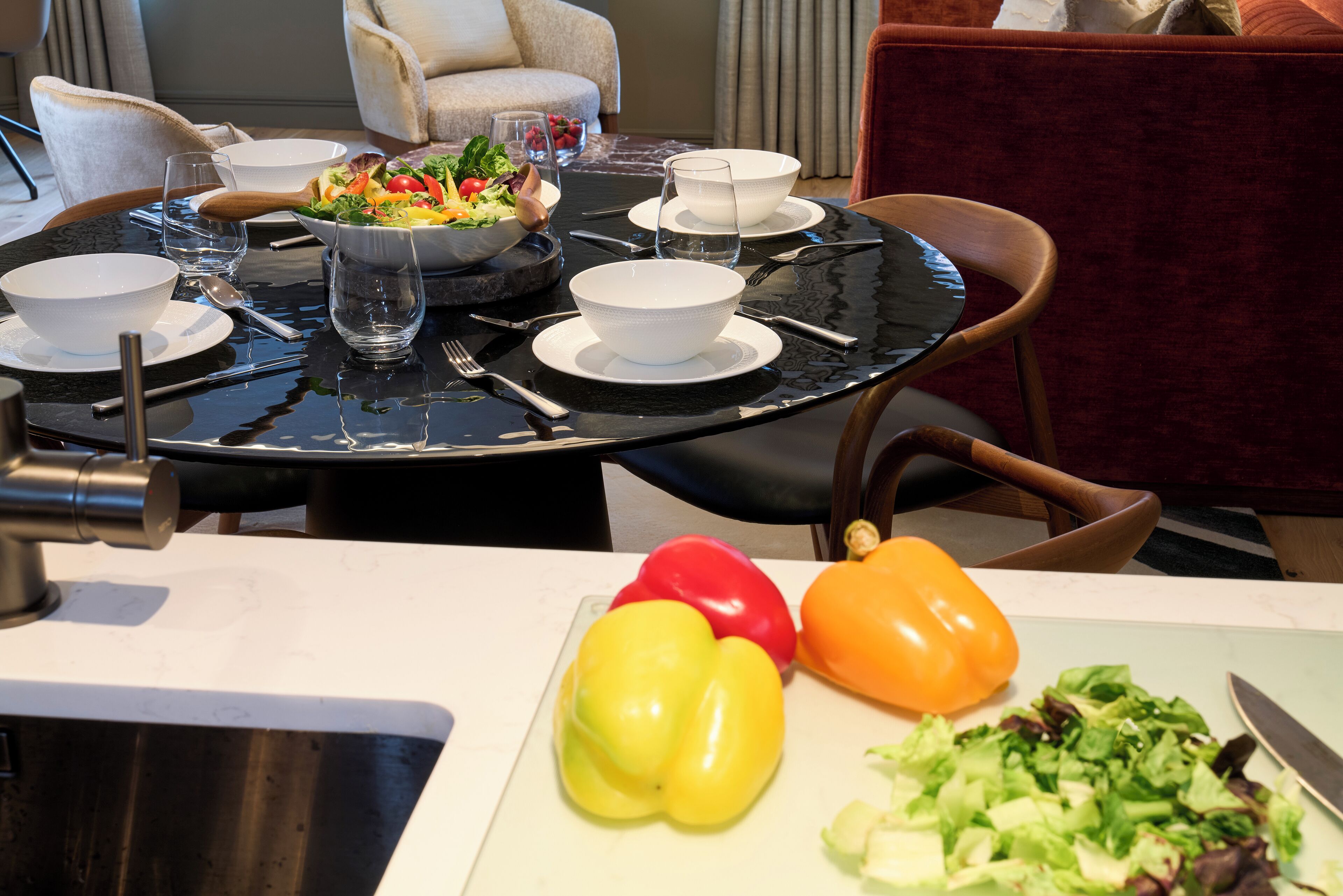 A dining table set with white bowls, plates, and cutlery, a bowl of salad, and a cutting board with vegetables.