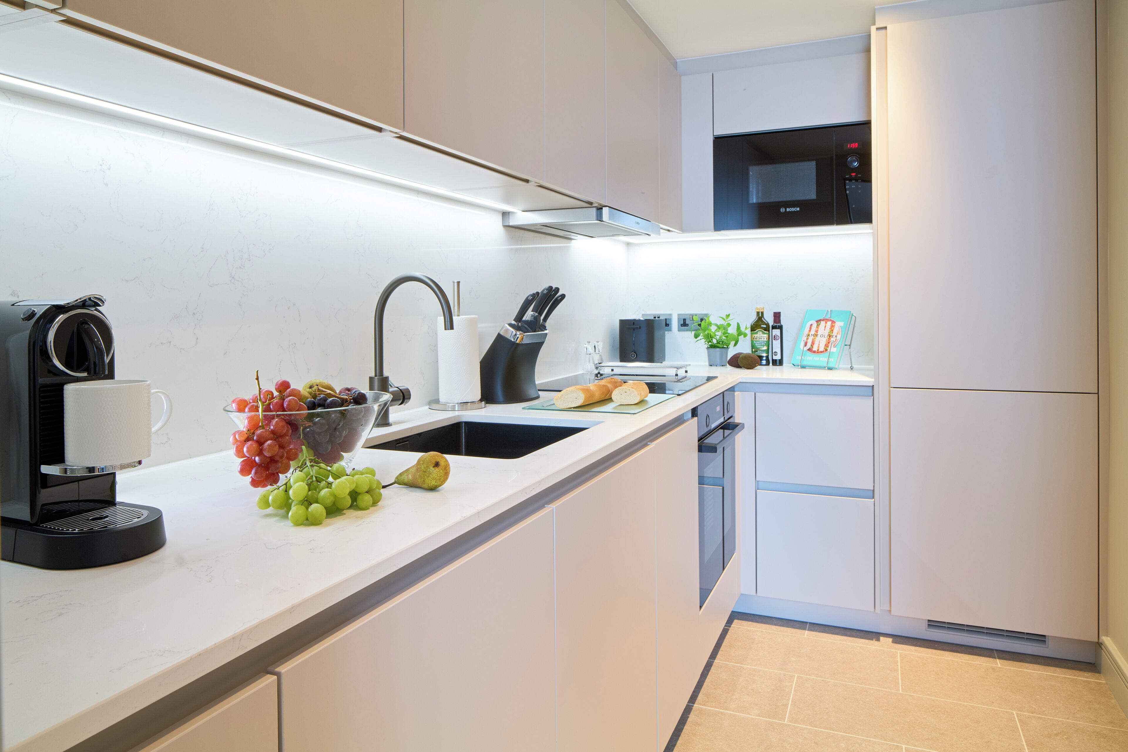 Uma cozinha moderna com máquina de café integrada, pia, micro-ondas e frigorífico.