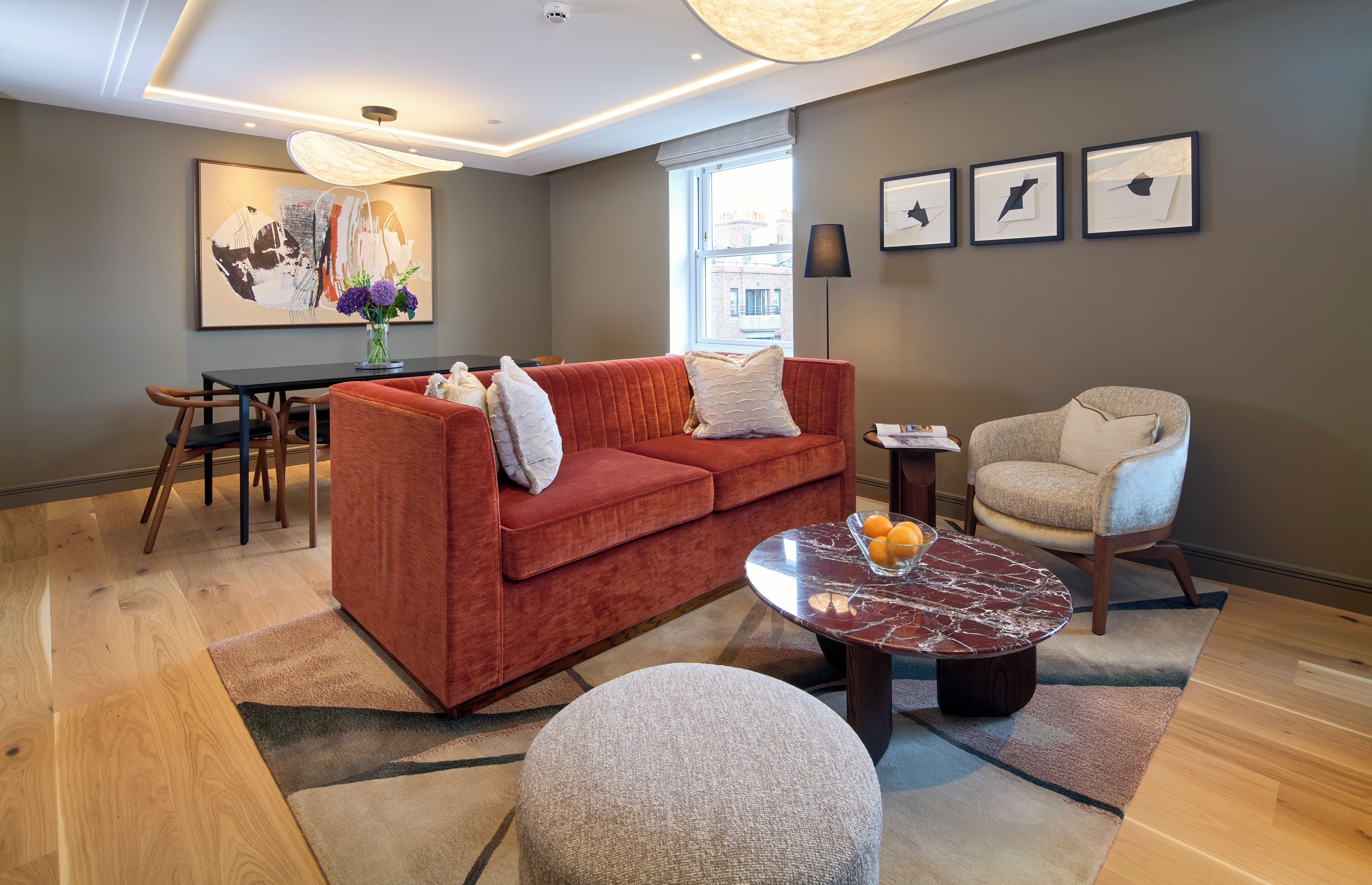 A modern living room with a red sofa, a beige armchair, a marble coffee table, and a dining area with a wooden table and chairs.
