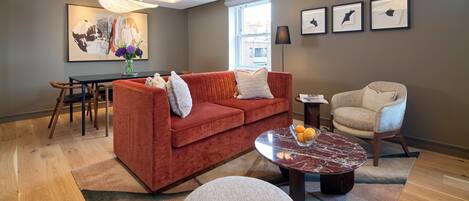 A modern living room with a red sofa, a beige armchair, a marble coffee table, and a dining area with a wooden table and chairs.
