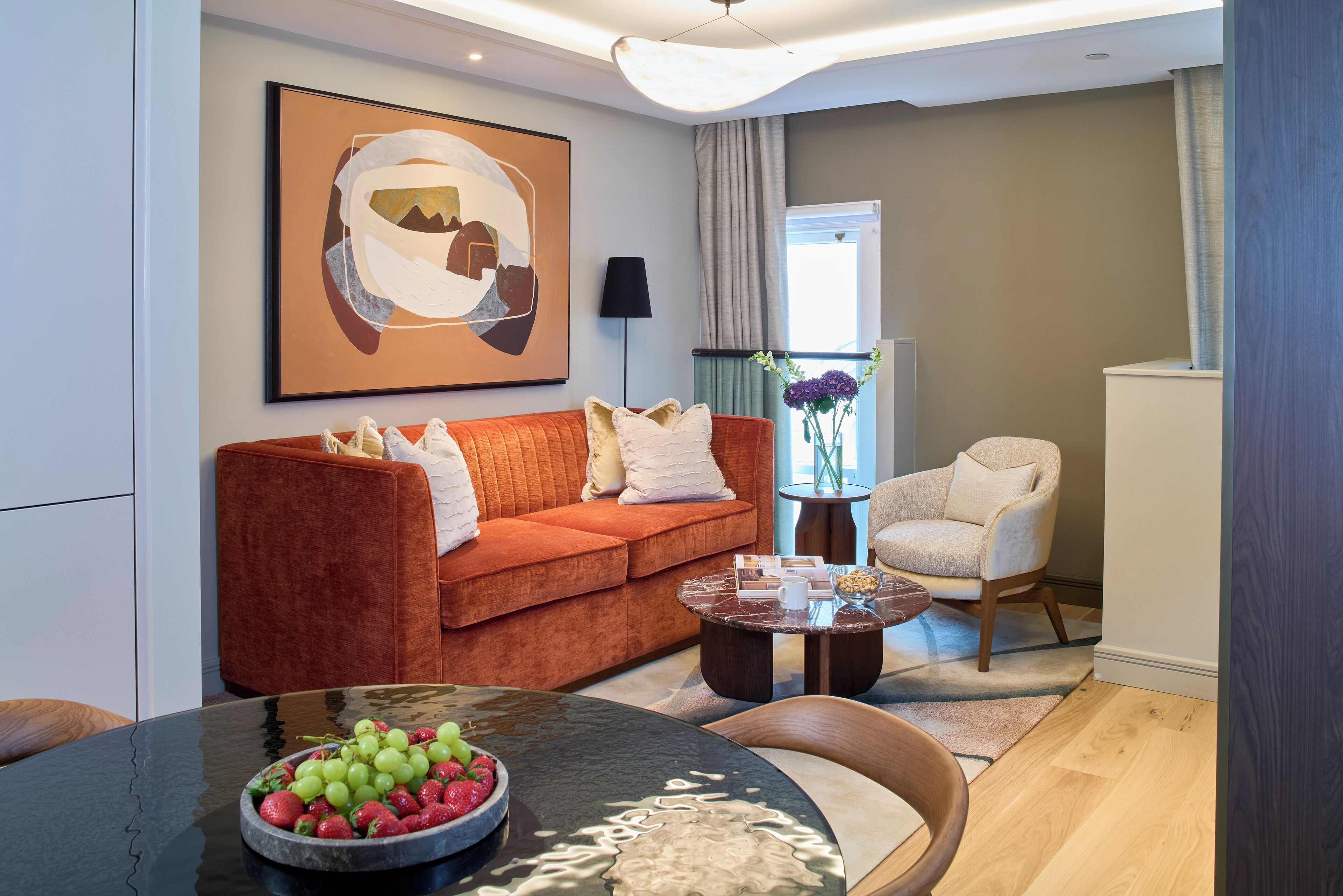 A modern living room with a sofa, armchair, coffee table, and a bowl of fruit.