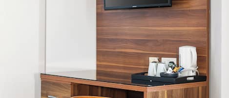 A modern office space with a built-in desk, a chair, a flat-screen TV, and a coffee machine.