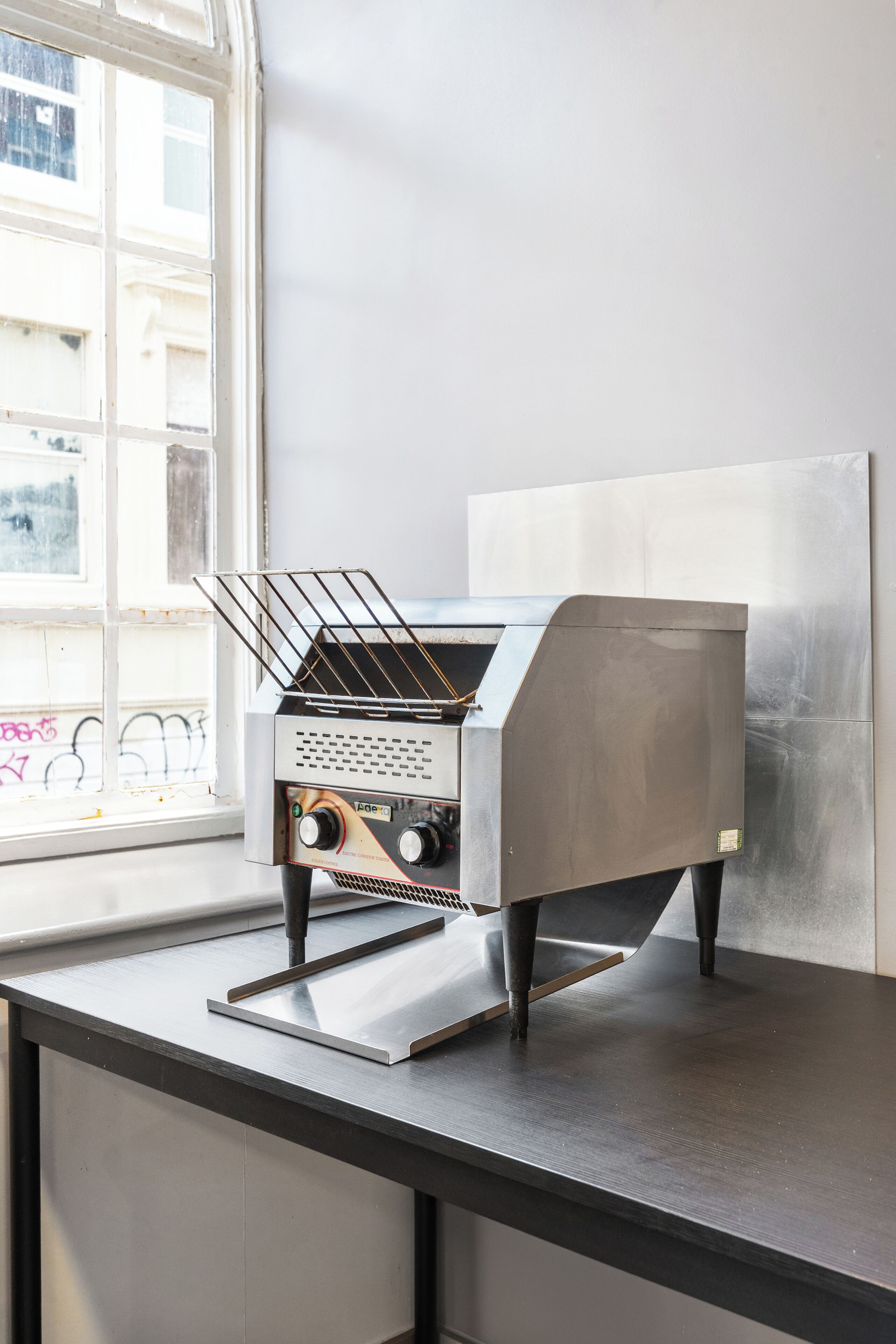 A kitchen with a stainless steel stove, a window with a view of the street, and a metal rack.