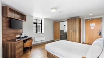 A hotel room with a bed, a desk with a television, a window, and a wardrobe.