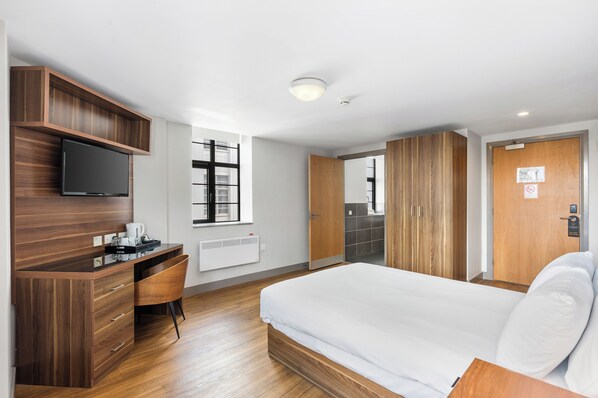 A hotel room with a bed, a desk with a television, a window, and a wardrobe. - The Mitre Hotel Brighton (Brighton)