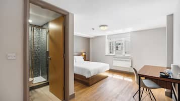 A hotel room with a bed, a desk, a chair, a shower, and a window.