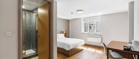 Ein Hotelzimmer mit Bett, Schreibtisch, Stuhl, Dusche und Fenster.