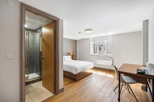 Habitación de hotel con cama, escritorio, silla, ducha y ventana.