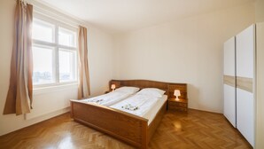A bedroom with a wooden bed, a nightstand, a lamp, a window with curtains, and a wardrobe. - Hostel Foster (Marianske Lazne)