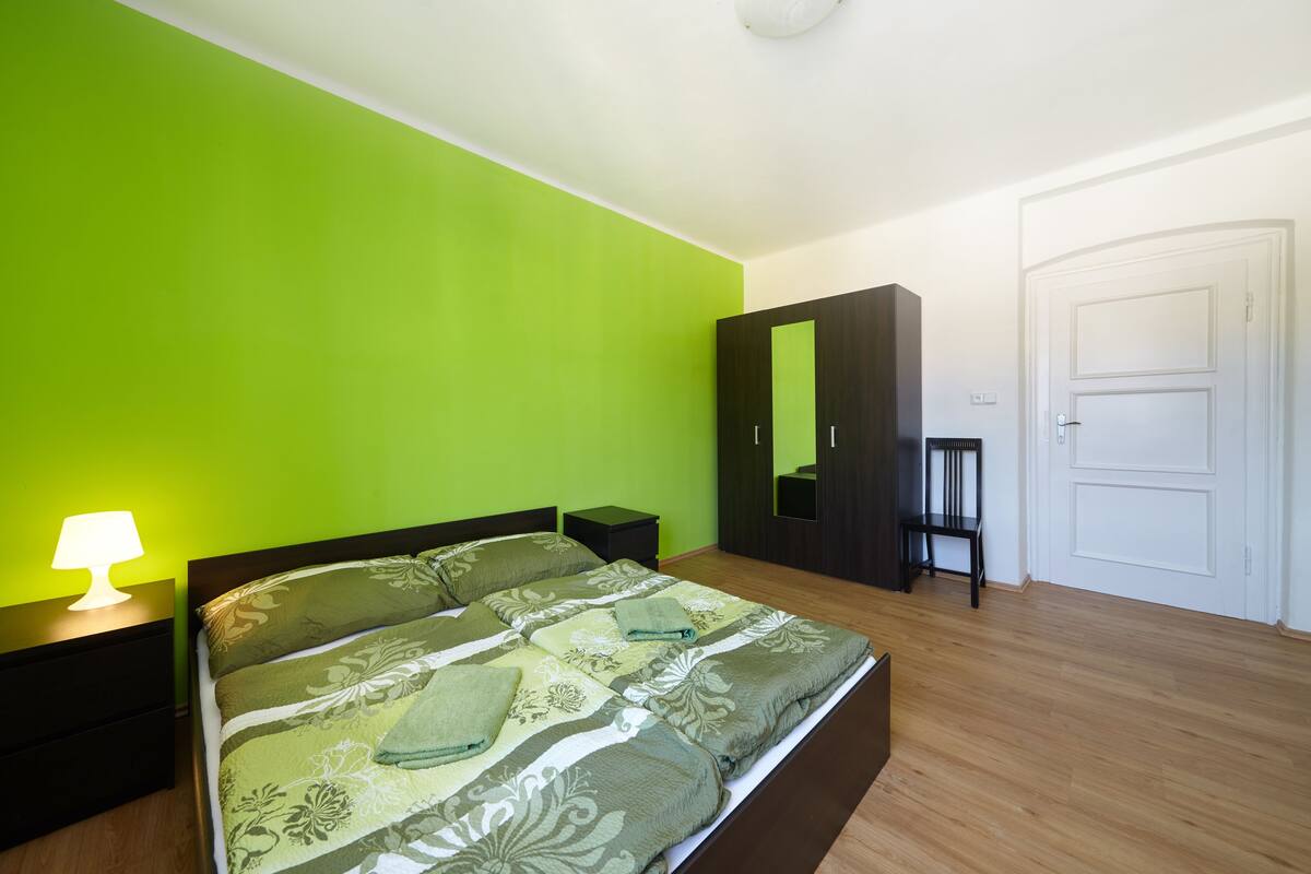 A bedroom with a bed, a nightstand, a lamp, a wardrobe, and a door.