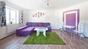 A modern living room with a sectional sofa, a white coffee table, a green rug, and a purple accent wall. - Hostel Foster (Marianske Lazne)