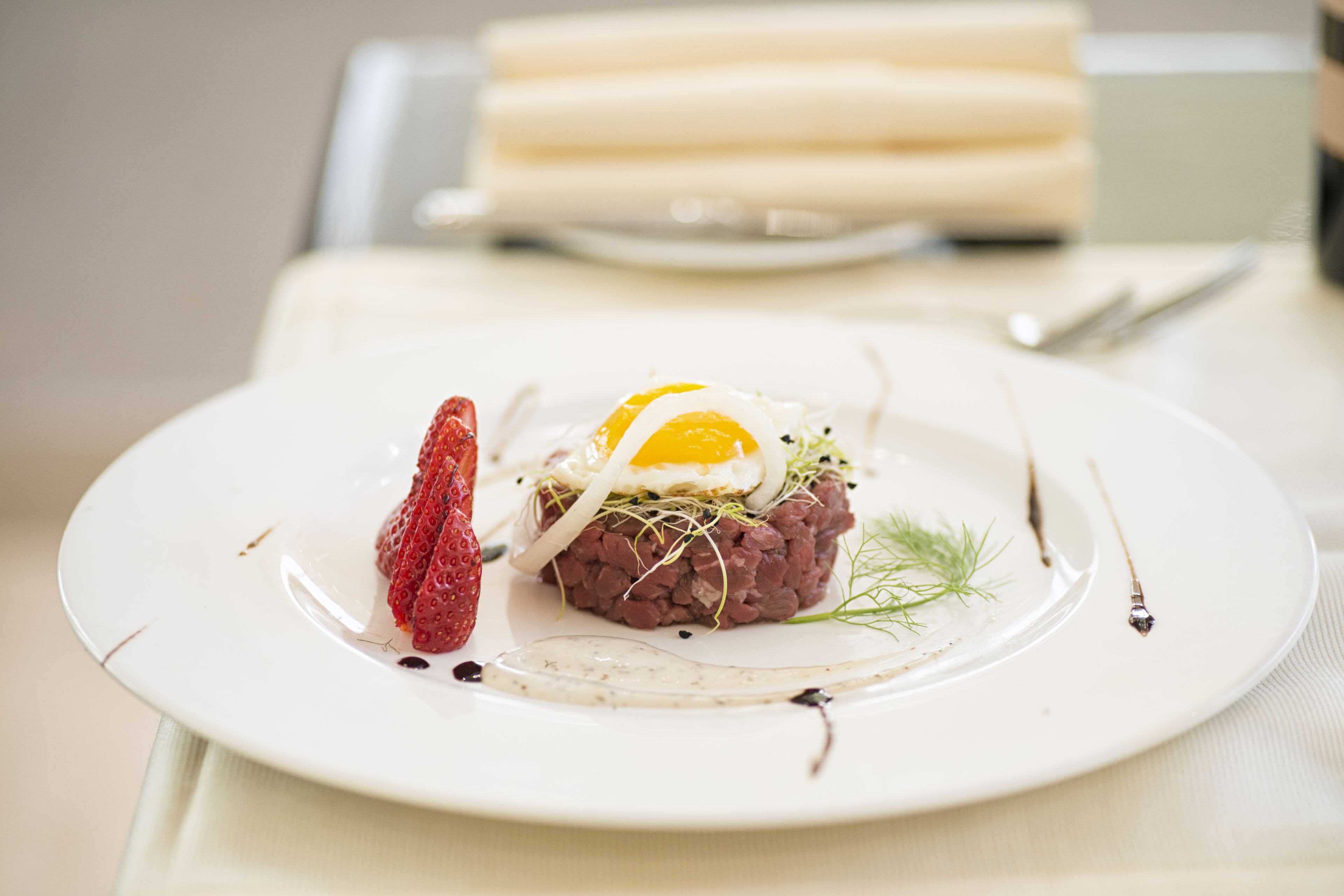 Um prato com uma porção de steak tartare, uma morango e um ovo pochê.