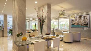 A modern hotel lobby with a glass table displaying breakfast items, a large vase with flowers, and a sign reading "THE". - Simon Hotel (Pomezia)