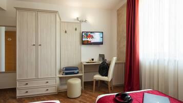 Ein Hotelzimmer mit Bett, Schreibtisch, Laptop, Fernseher, Kleiderschrank und Stuhl.