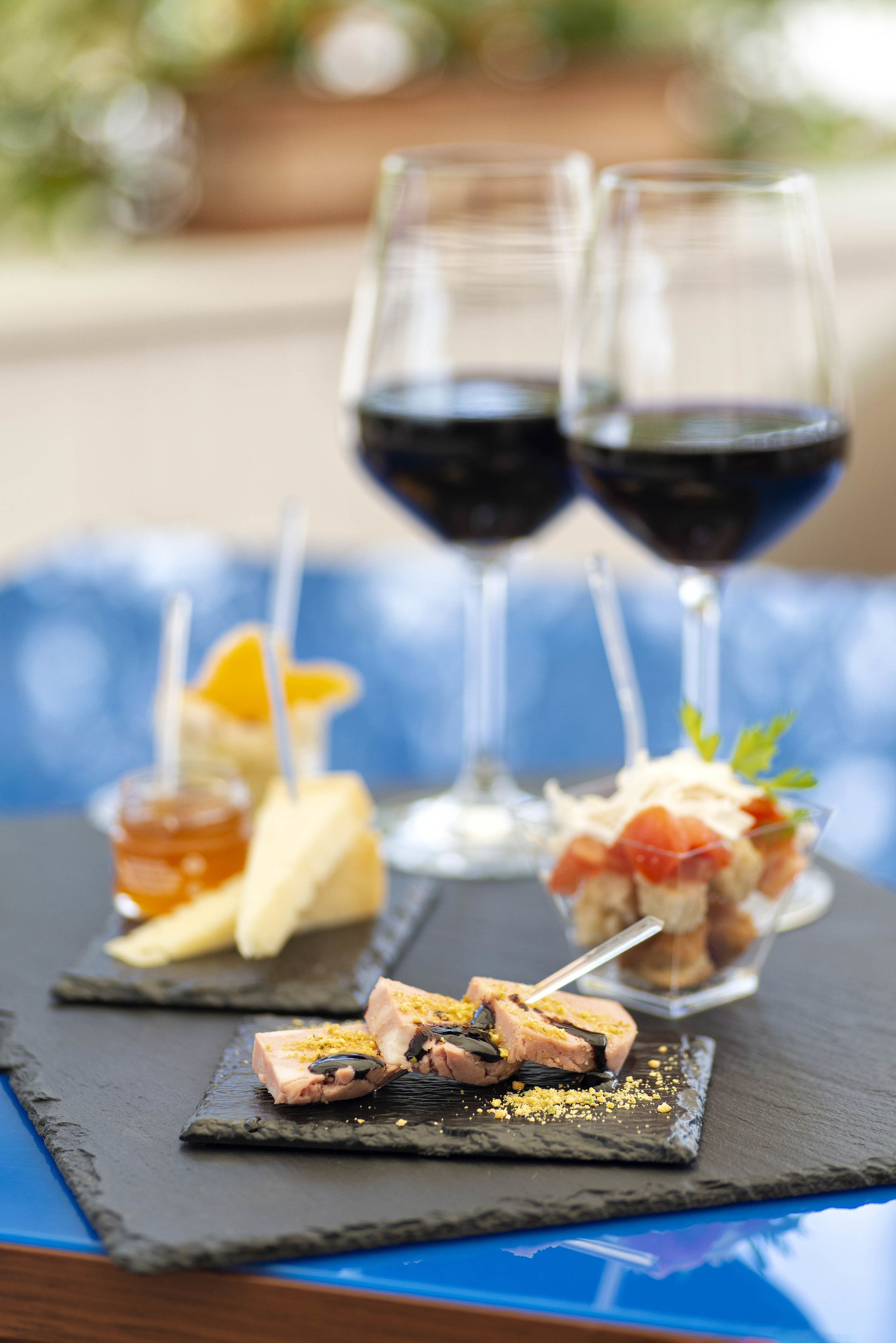A table with three dishes and two glasses of red wine.