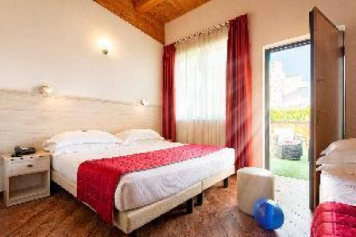 A bedroom with a bed, a nightstand, a window with curtains, and a door leading outside.