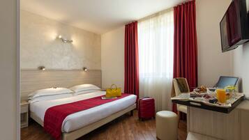 Une chambre d’hôtel avec un lit, une table de chevet, un bureau avec un petit-déjeuner, une valise et un téléviseur.