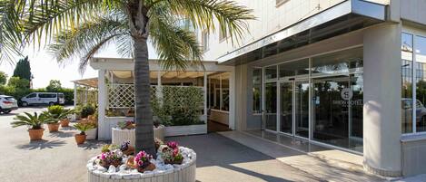 Un hotel moderno con entrada cubierta, plantas en macetas y una palmera.