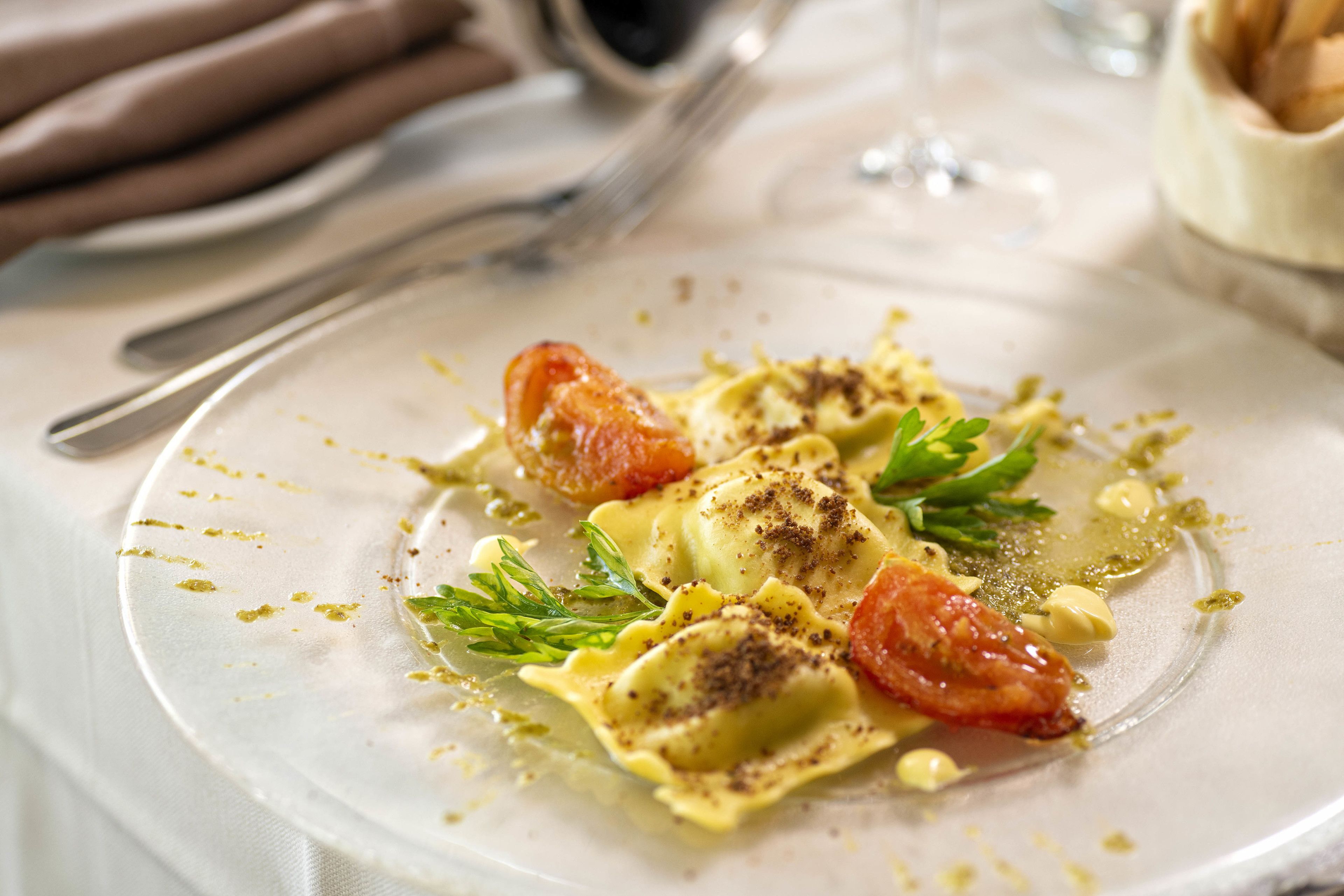 A plate of ravioli with tomato and pesto garnish.