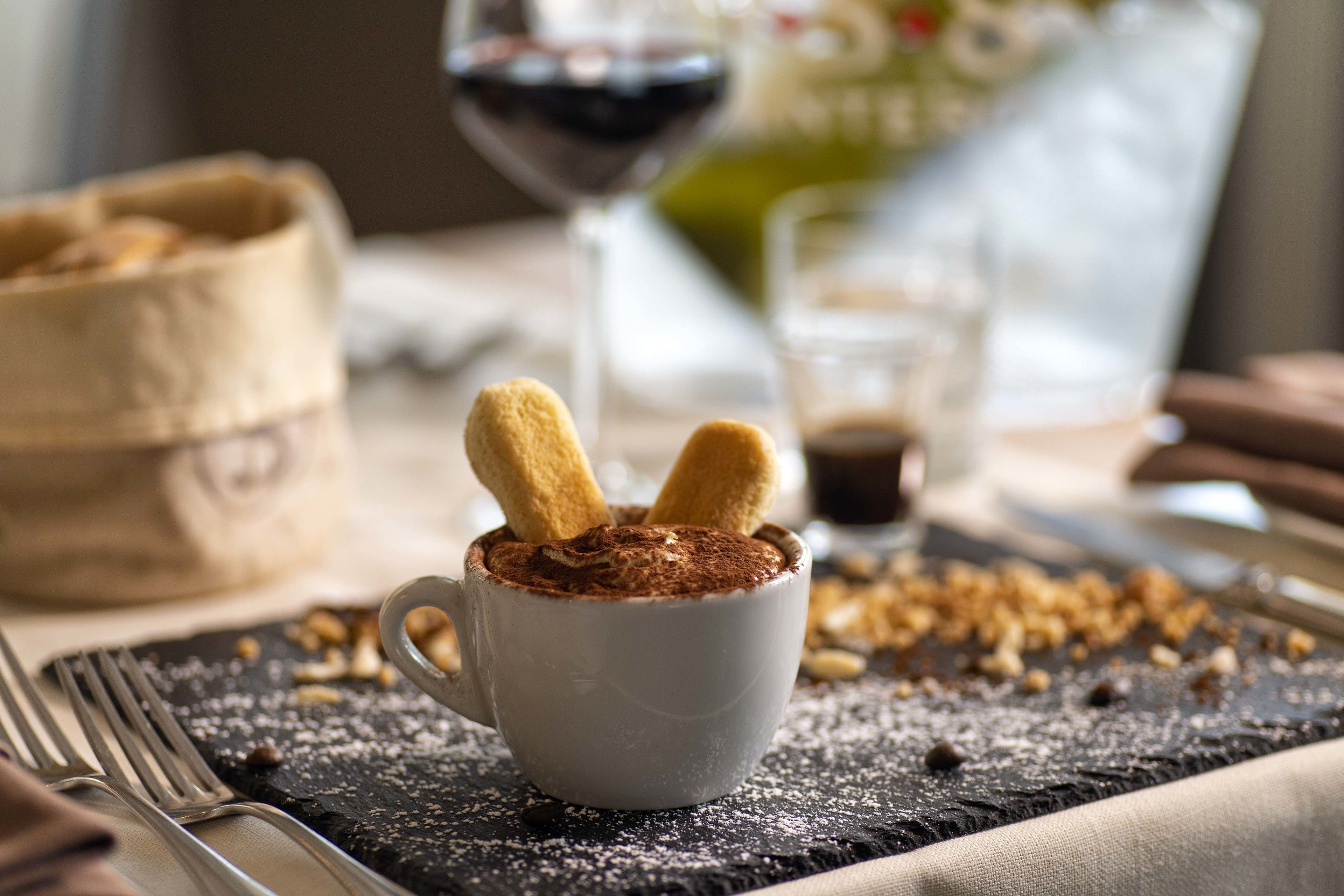 Una tazza di cioccolata calda con marshmallow su un tavolo, con tovagliolo, forchetta e un bicchiere di vino.