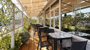 An outdoor patio with tables and chairs, covered by a canopy, and surrounded by greenery. - Simon Hotel (Pomezia)
