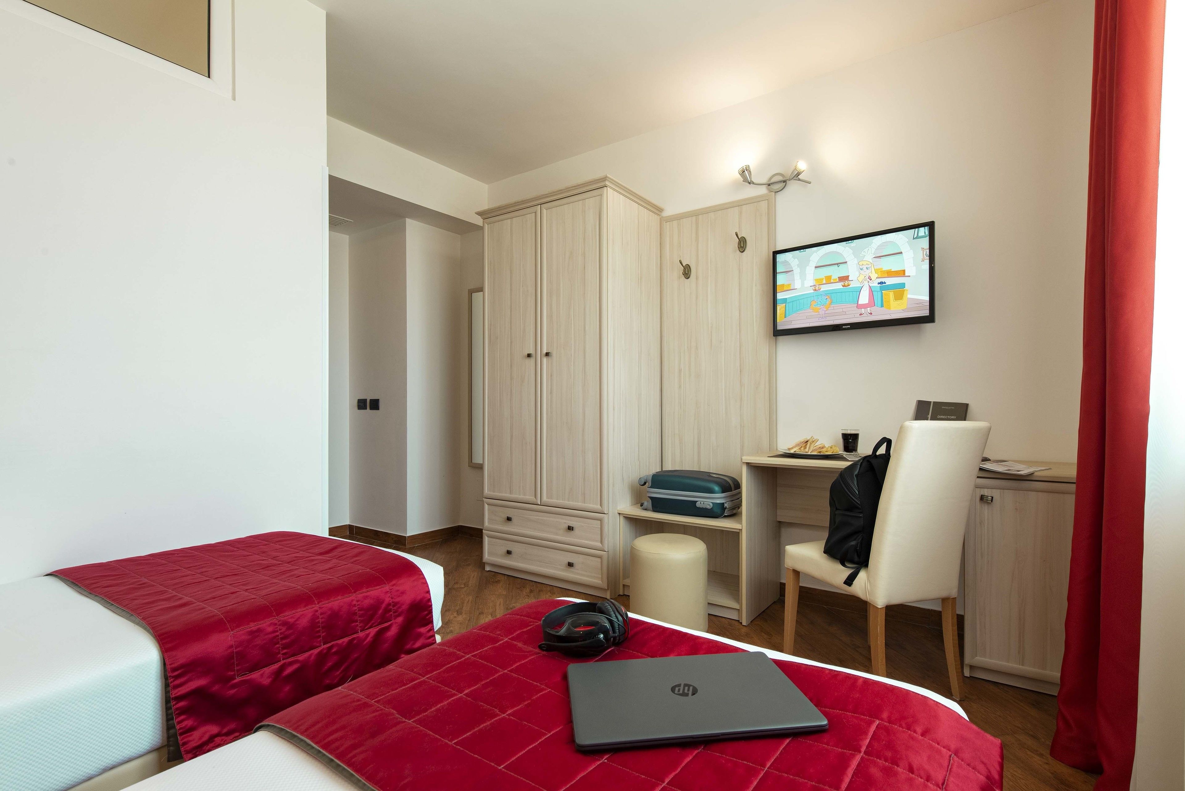Ein Schlafzimmer mit zwei Betten, einem Schreibtisch, einem Stuhl, einem Laptop und einem Fernseher.