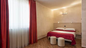 Ein Hotelzimmer mit Holzboden, einem Bett mit roter Bettwäsche, einem Nachttisch und einem Beistelltisch.