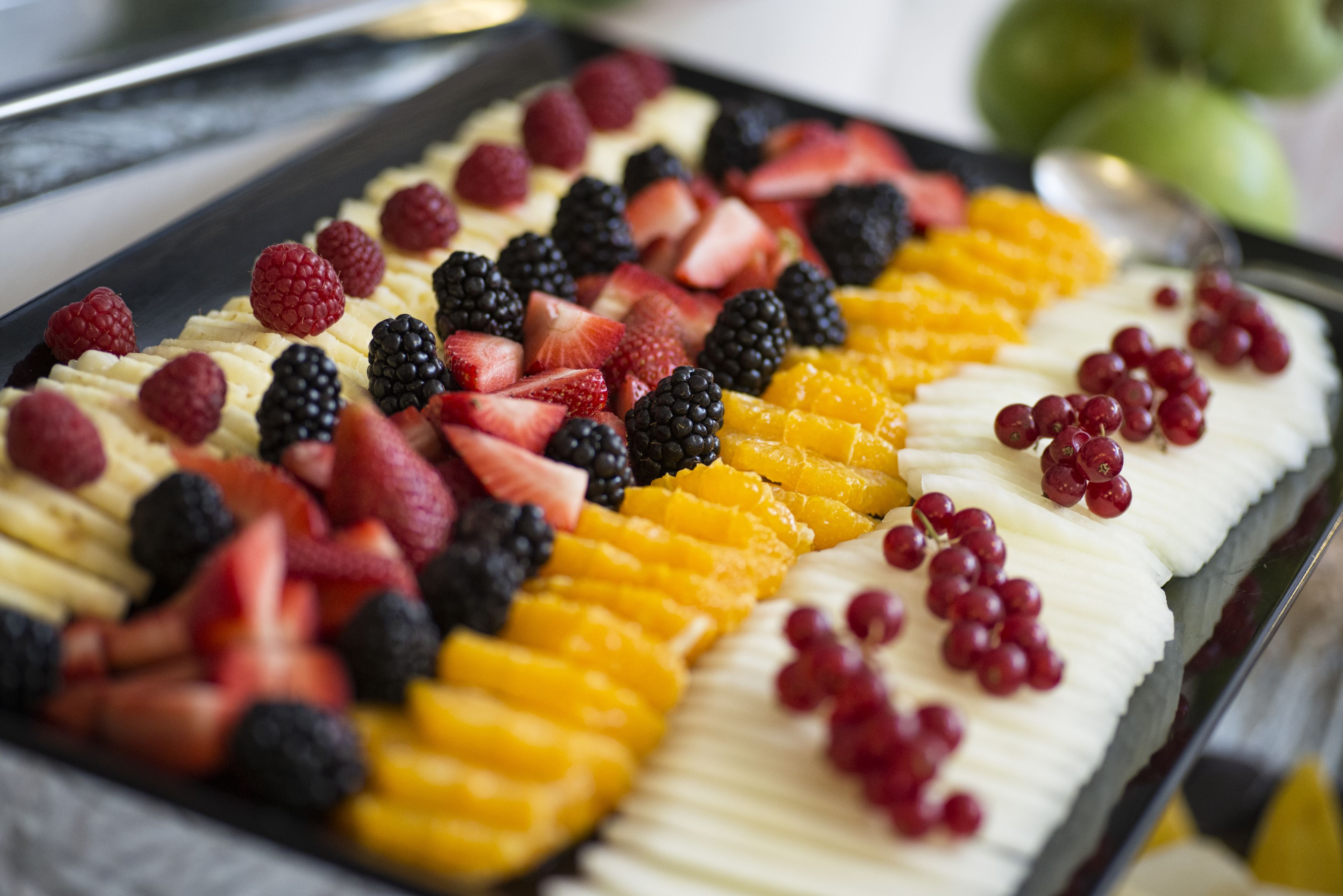 Een schaal met diverse soorten fruit, waaronder aardbeien, bramen, frambozen en mandarijnen.