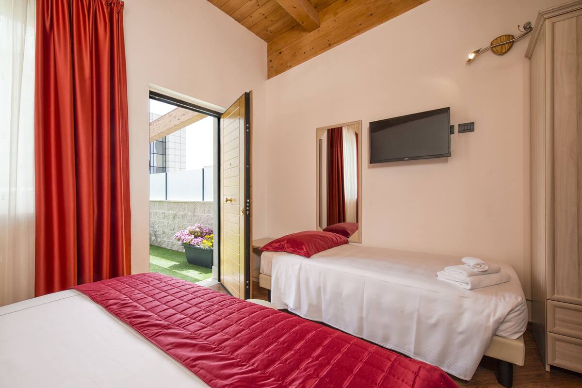 A bedroom with two beds, a TV, and a view of a balcony with flowers.
