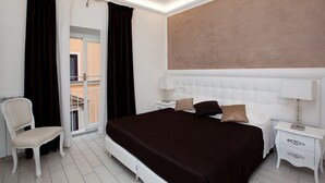 Un dormitorio con una cama grande, una mesita de noche, una silla y vistas al balcón exterior por una puerta corrediza.