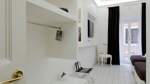 Una habitación moderna y bien iluminada con un escritorio de vidrio, una silla blanca, un sofá marrón y un televisor en la pared.