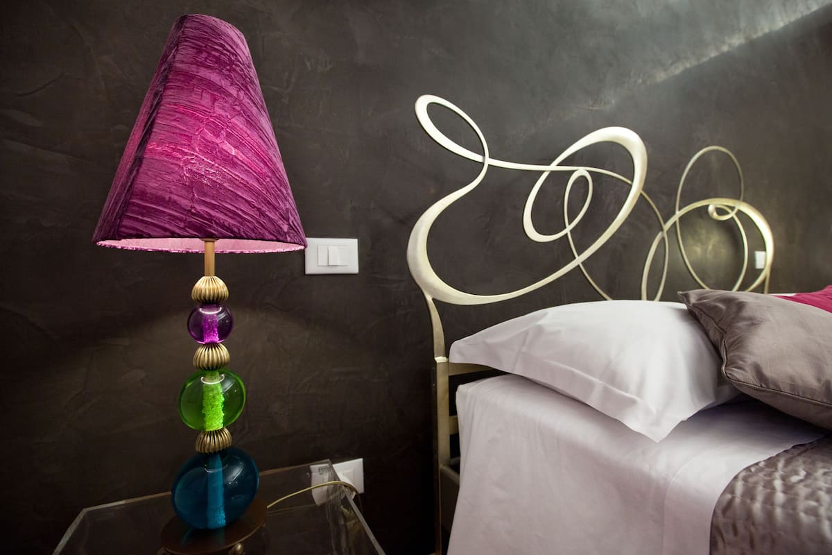 En seng med hvidgengivet knægløb, et natbord med lampe, og en vægkontakt.