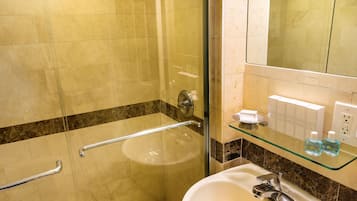 A bathroom with a glass-enclosed shower, a white sink, and a glass shelf with toiletries.