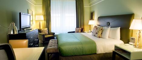 Una camera d'albergo con un letto, una scrivania, una sedia, una televisione e una lampada.