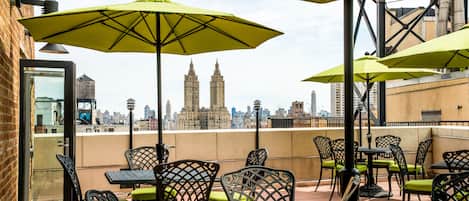 A rooftop terrace with outdoor seating, including tables and chairs, and large umbrellas providing shade.