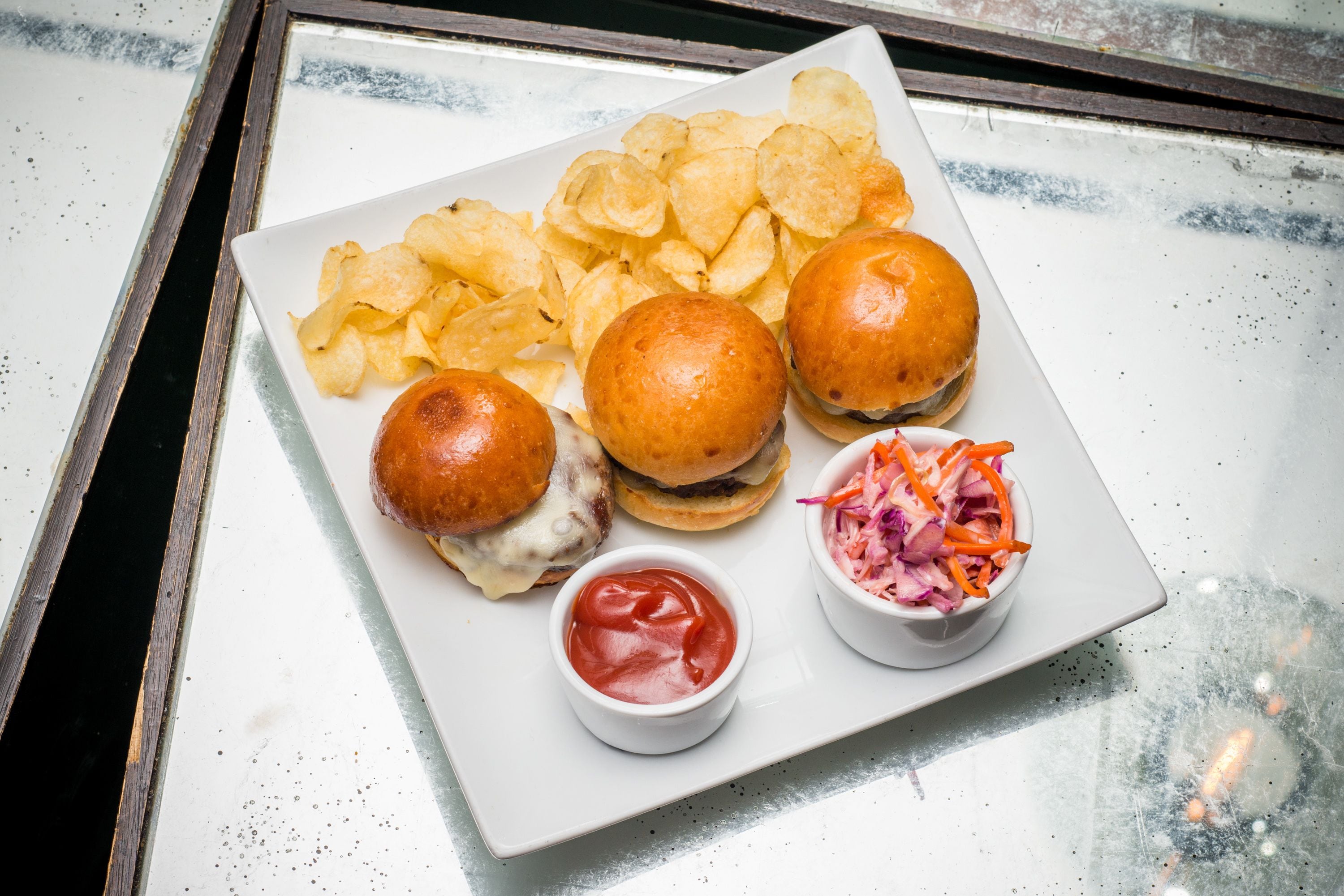 Une assiette avec deux hamburgers, une portion de frites et un petit bol de salade de chou.