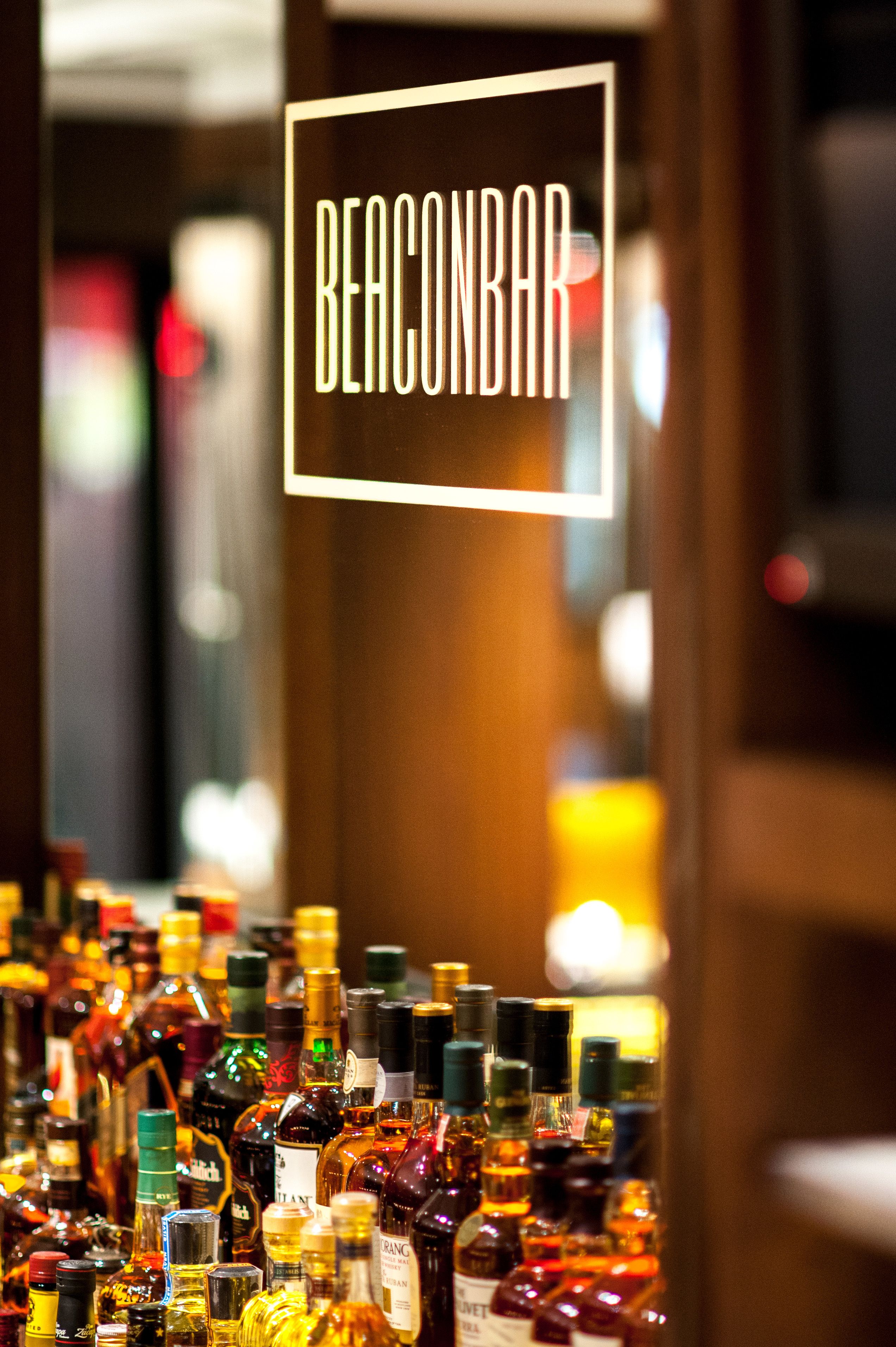 A bar with a sign reading "BEACONBAR" and a variety of liquor bottles on display.