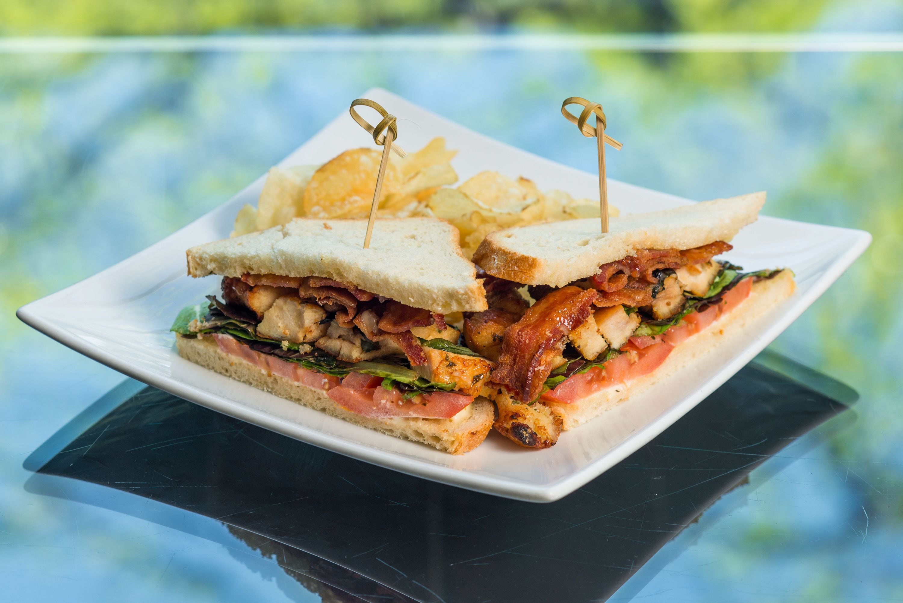 A sandwich with a toothpick on a plate, accompanied by chips.