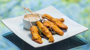 Um prato de espetinhos com molho para acompanhar, sobre uma mesa de vidro.