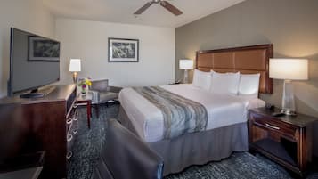 A hotel room with a large bed, a desk, a chair, a TV, and a ceiling fan.