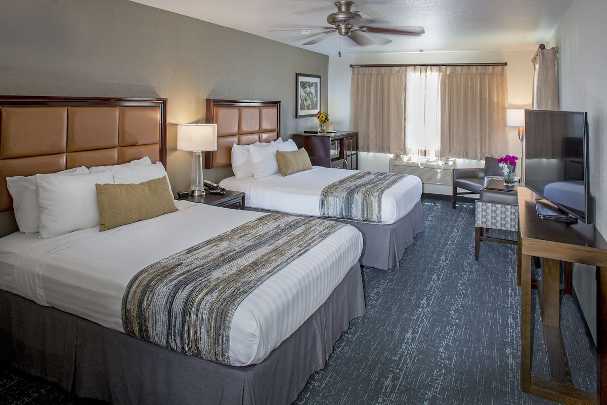 A hotel room with two beds, a desk, a TV, and a ceiling fan.