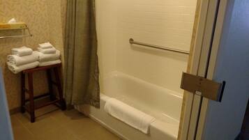 A bathroom with a bathtub, a towel rack with folded towels, a tissue box on a shelf, and a curtain.