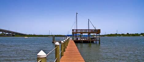 A wooden pier extending into calm water, with a docked boat and a bridge in the background.
