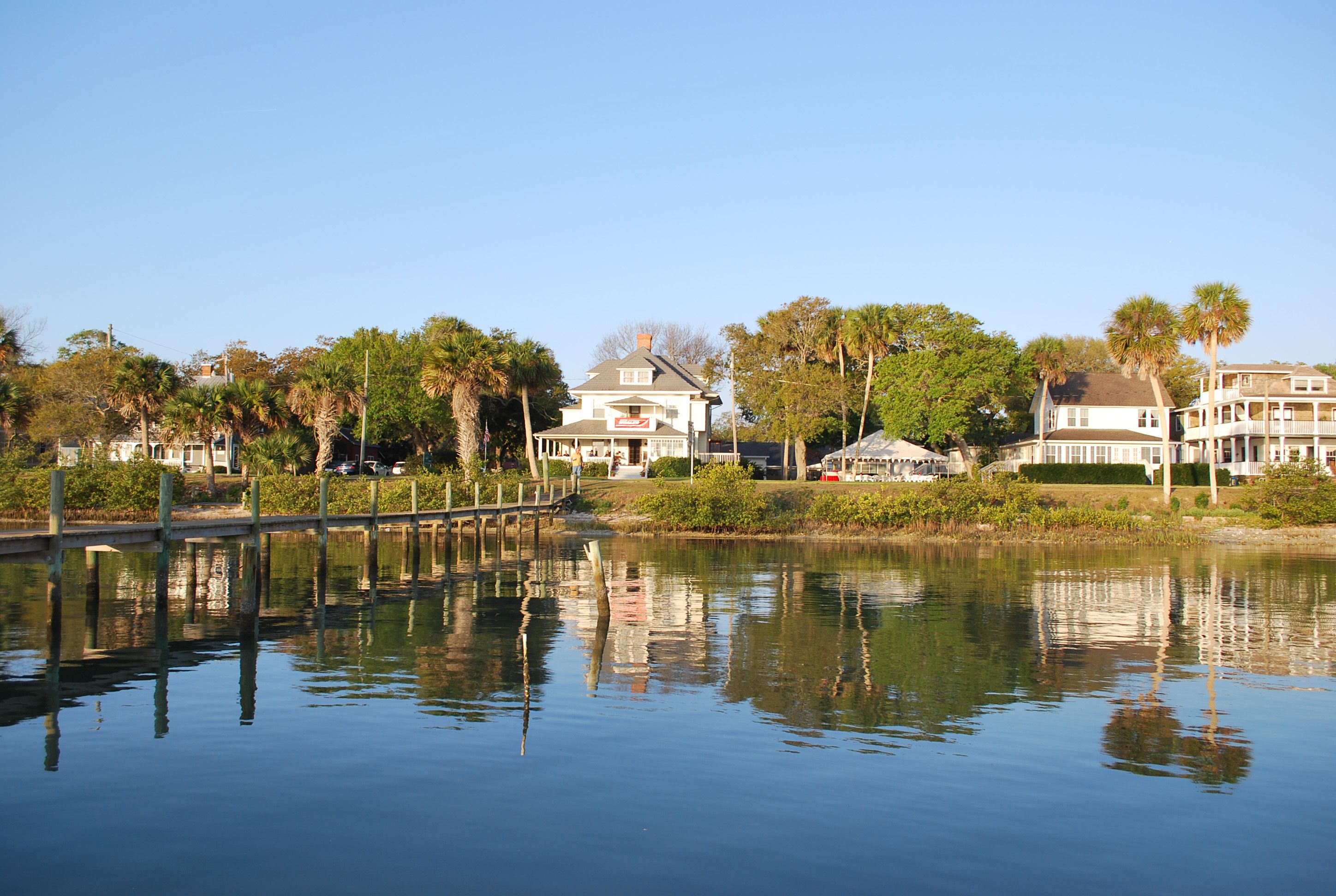 A waterfront property with a dock, a large house, and surrounding palm trees.