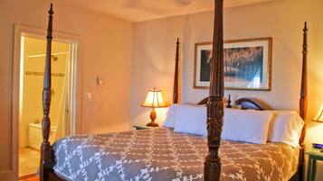 A four-poster bed with a patterned bedspread, a bedside lamp, and a framed picture on the wall.