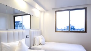 Une chambre d’hôtel avec deux lits simples, une grande fenêtre donnant sur la ville, un miroir et un design moderne au niveau du plafond.