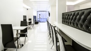 Une salle de conférence moderne et bien éclairée, avec une longue table, des chaises noires et un banc rembourré le long d’un des murs.