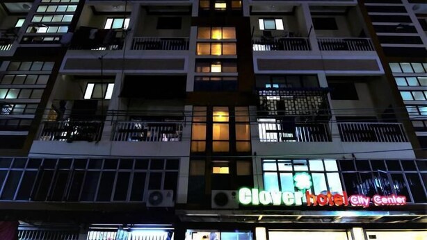 Un hôtel à plusieurs étages, doté de fenêtres et de balcons illuminés, et sur lequel on peut voir une grande enseigne indiquant « Clover Hotel ».