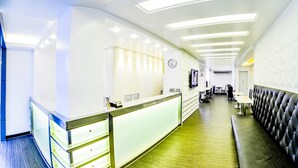 Un hall d’hôtel moderne avec un comptoir d’accueil, un espace salon et une horloge au mur.