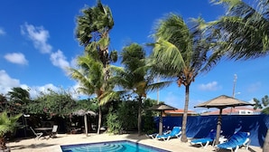 A rectangular swimming pool with clear blue water, surrounded by a sandy area with lounge chairs and palm trees. - Caribbean Chillout (Kralendijk)